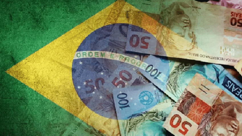 foto da bandeira do brasil com notas de 50 e 100 reais na direita da imagem sobreposta à bandeira.