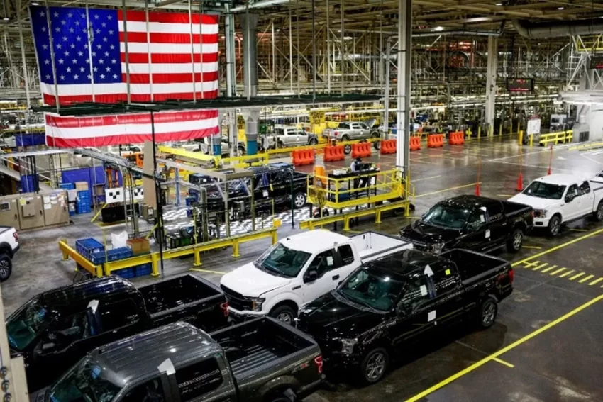 foto de uma fábrica de automóveis com a bandeira dos eua de fundo
